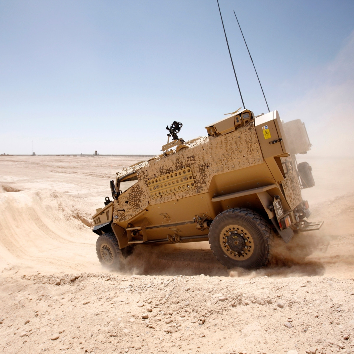 Foxhound armoured vehicle driving through desert terrain, kicking up dust