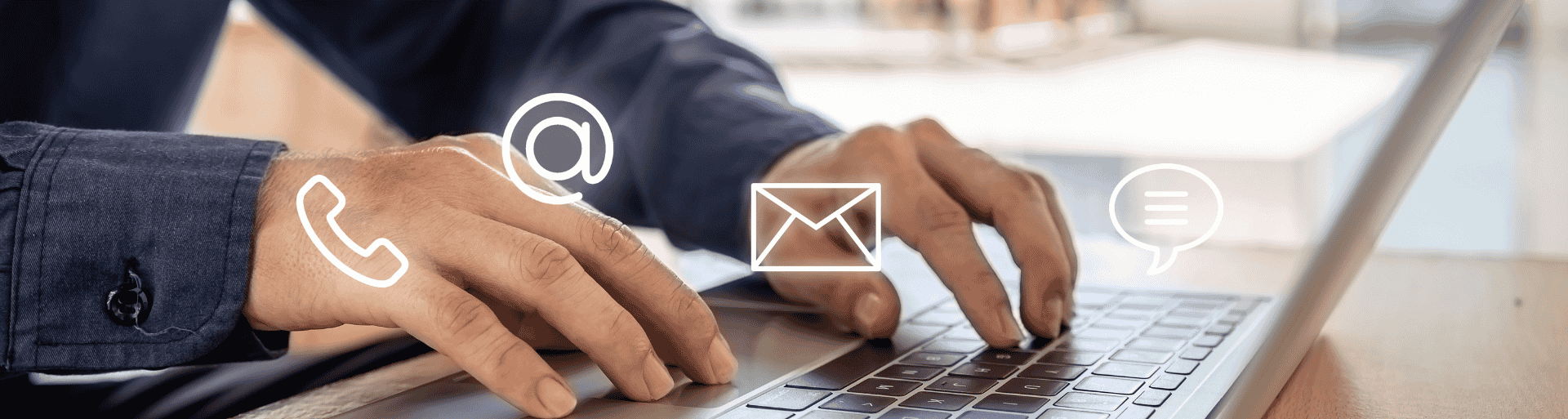 Person typing on a laptop with phone, email and @ contact icons